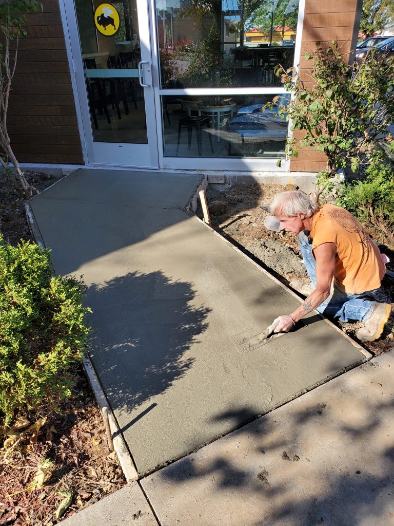 A professional worker smoothing freshly poured concrete for a sidewalk.